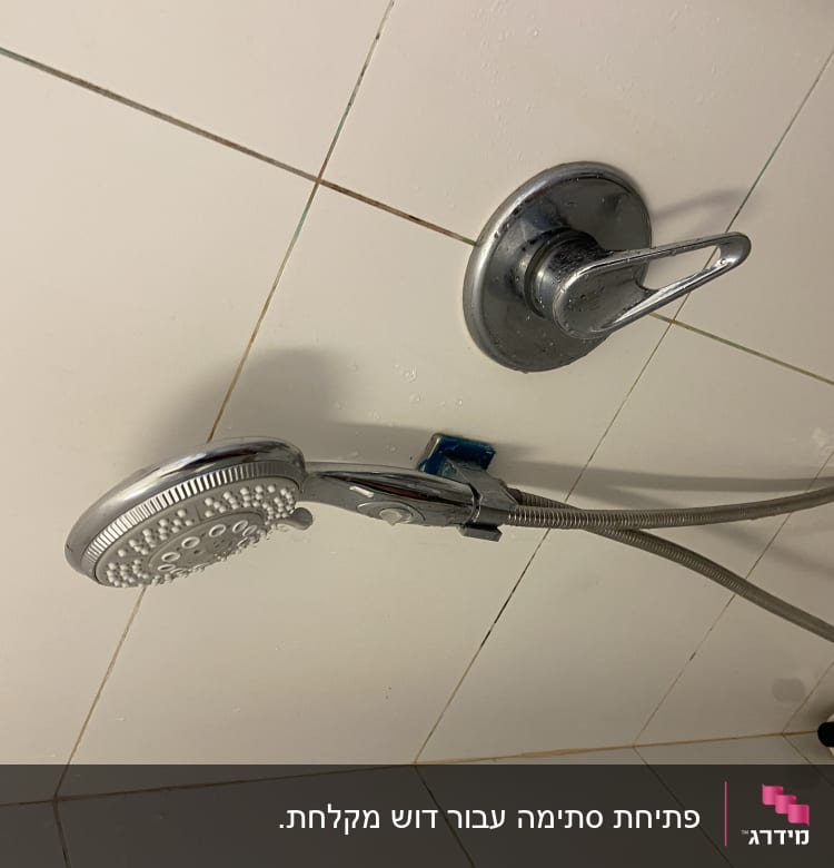 ראש מקלחת וכפתור מים על קיר אריחים